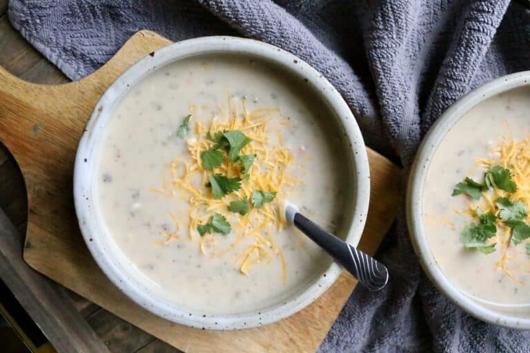 two bowls of creamy potato vegetable soup with cheese and parsley on top