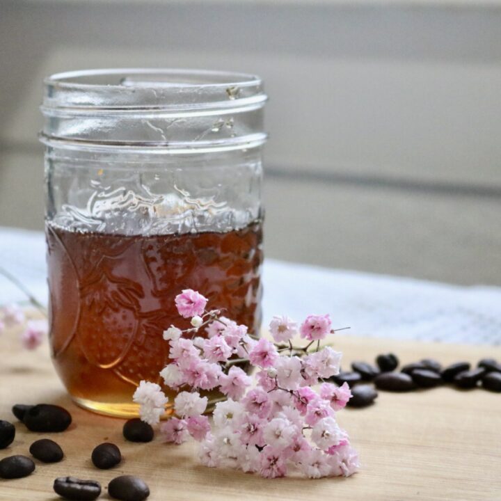 homemade coffee syrup in small jar with flowers and coffee beans scattered around it