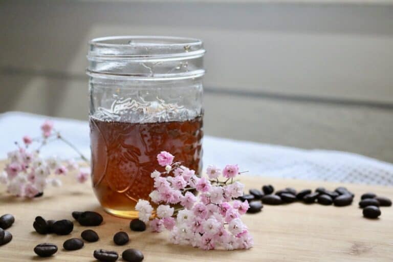 homemade coffee syrup in small jar with flowers and coffee beans scattered around it