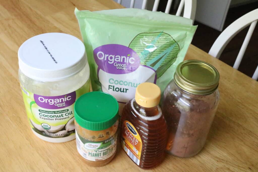 coconut flout, coconut oil, peanut butter, honey, and cocoa powder on a table