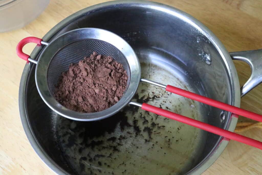 sifting cocoa powder into a small saucepan with coconut oil and honey in it