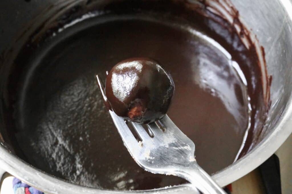dark chocolate covered peanut butter ball on a fork over a saucepan with chocolate sauce in it
