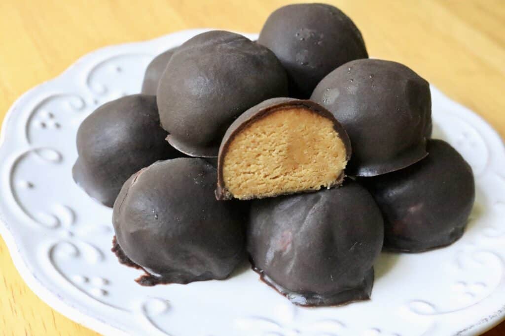 dark chocolate covered peanut butter balls on a white plate with one of them cut in half