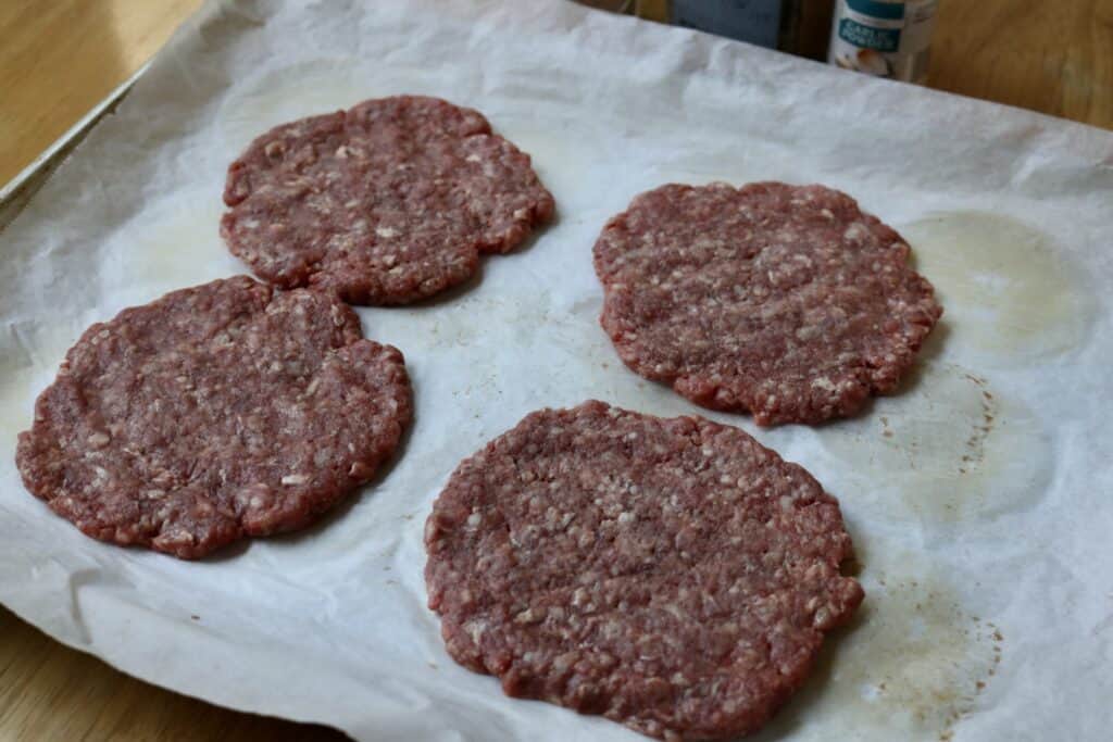 four burger patties on a parchment paper lined baking sheet