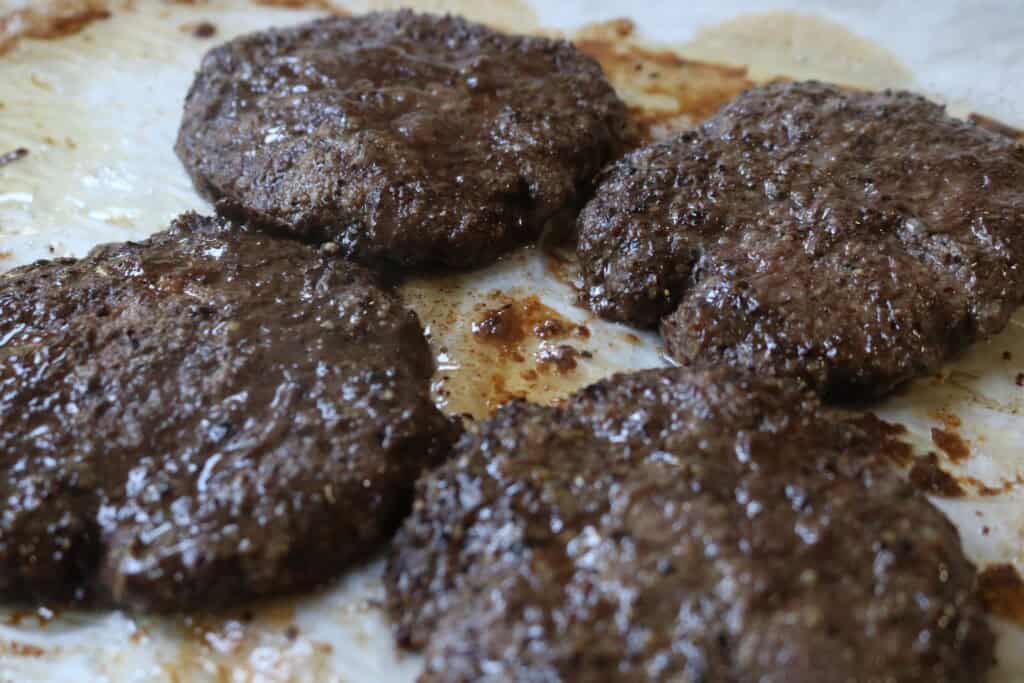 four cooked burger patties on a baking sheet