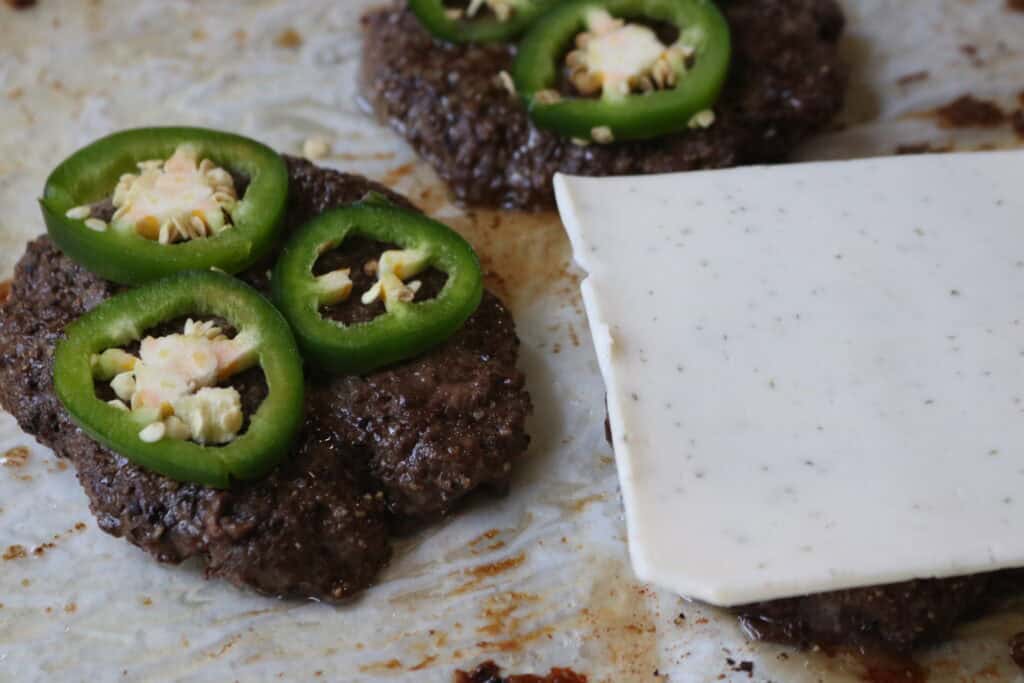 three burger patties with jalapeños and cheese on them