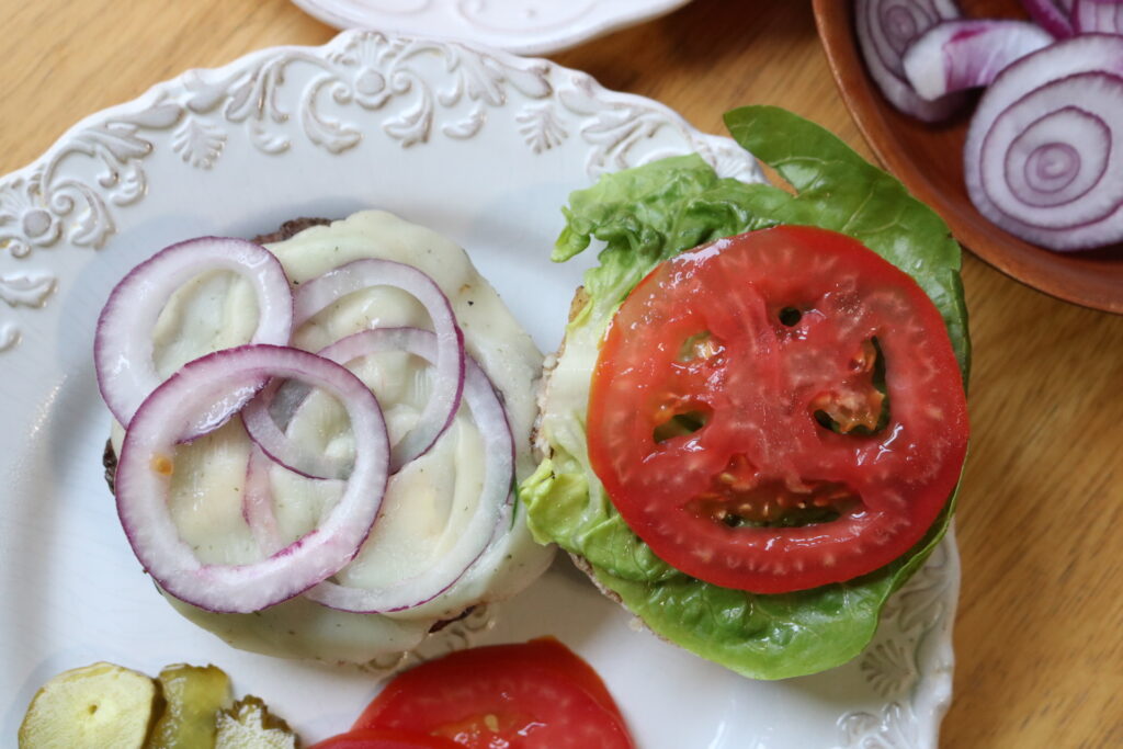 top view of hamburger with cheese, onions, lettuce, and tomatoes on a white plate
