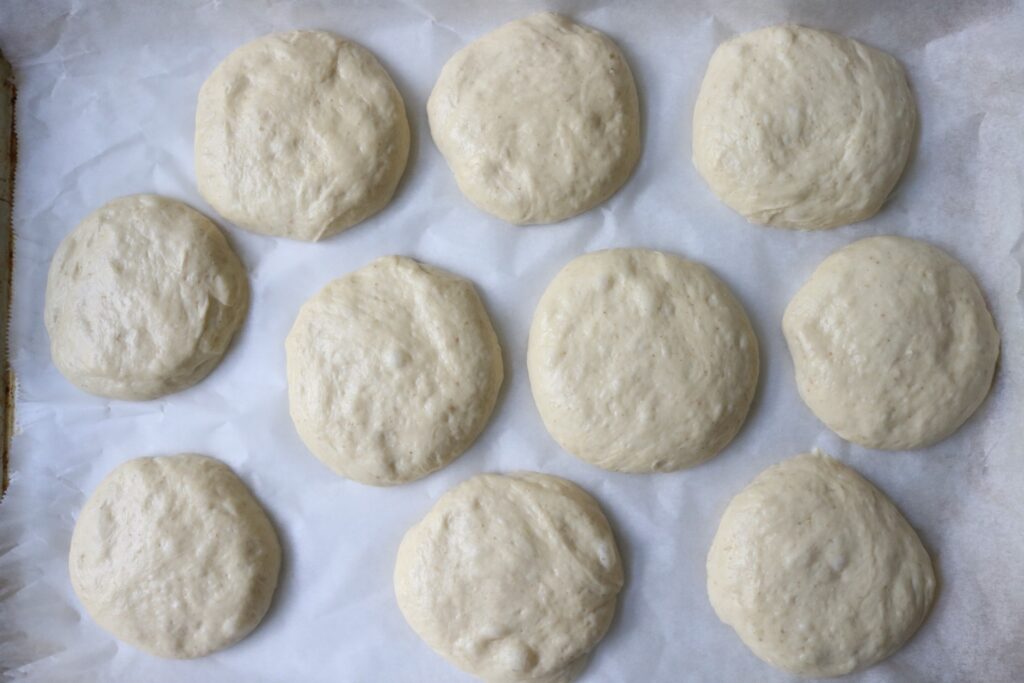 10 uncooked sourdough burger buns on a parchment paper lined baking sheet