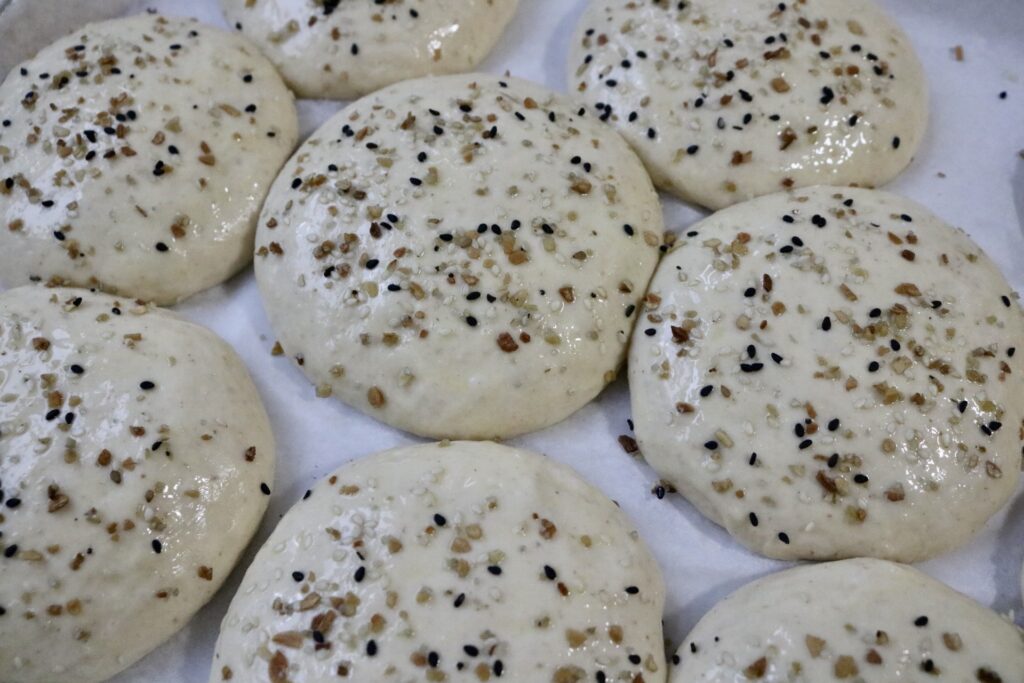 uncooked buns on a baking sheet with seeds sprinkled on them