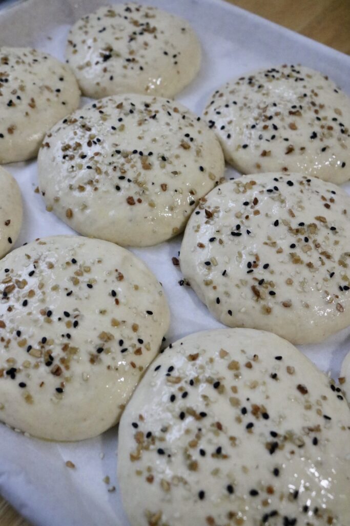 uncooked hamburger buns on a cookie sheet with seeds on top