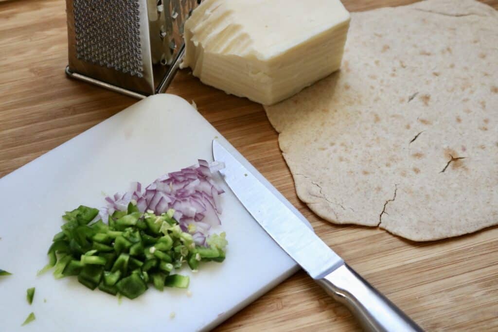 onion and green peppers cut up on a board with block of cheese and tortilla in the backround