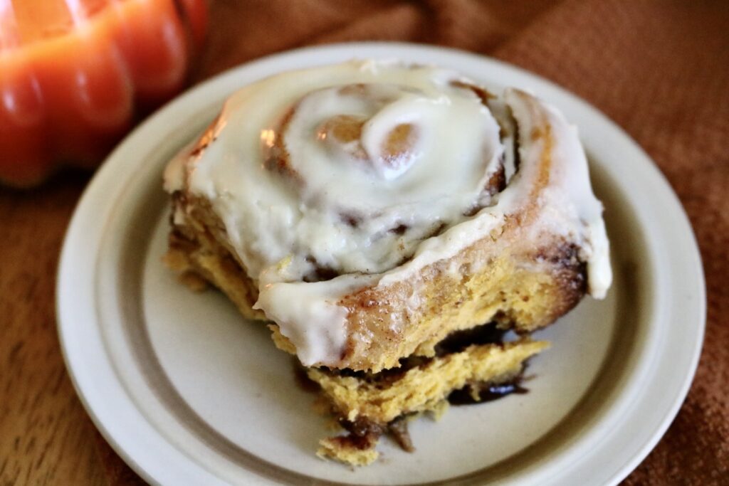 1 sourdough pumpkin cinnamon roll on a plate with a candle in the backround