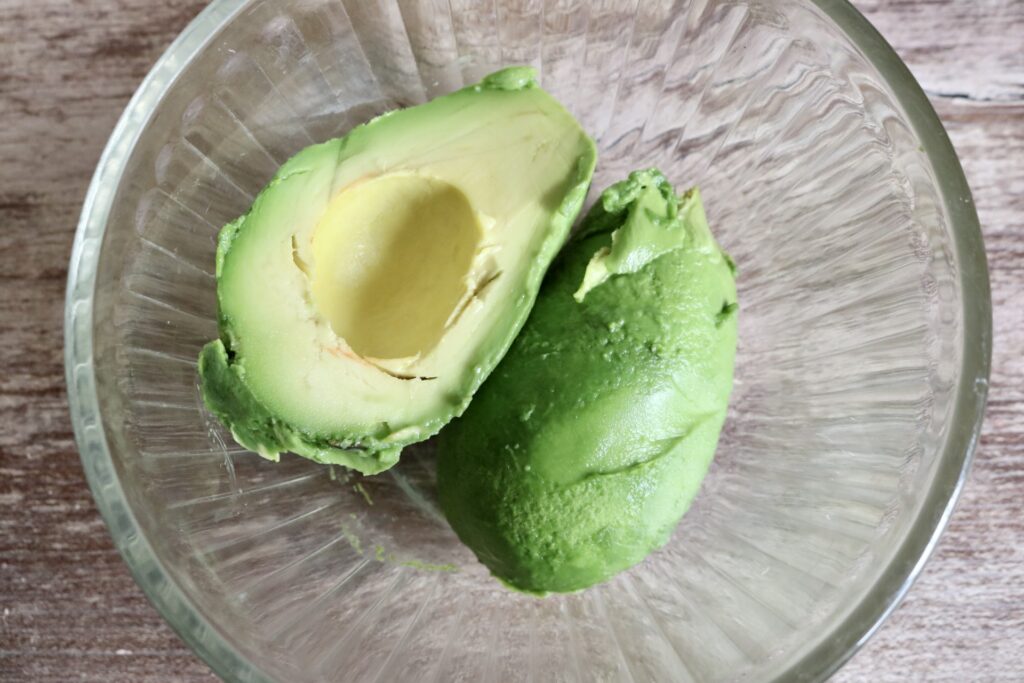 peeled and pitted avocado cut in half in a glass bowl