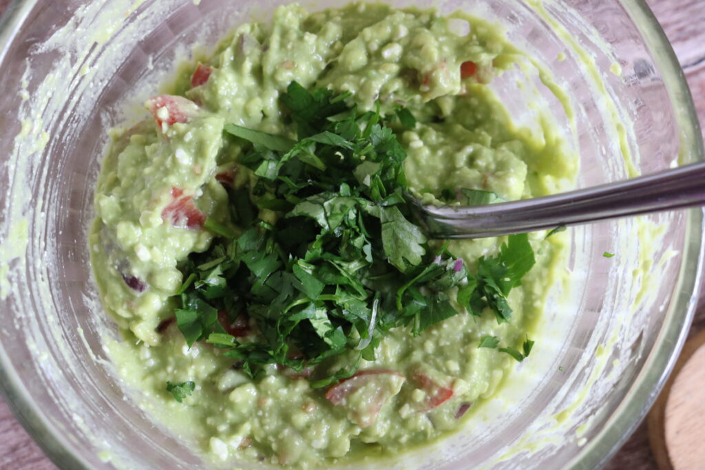 guacamole dip with fresh cilantro on top in bowl being mixed with a fork