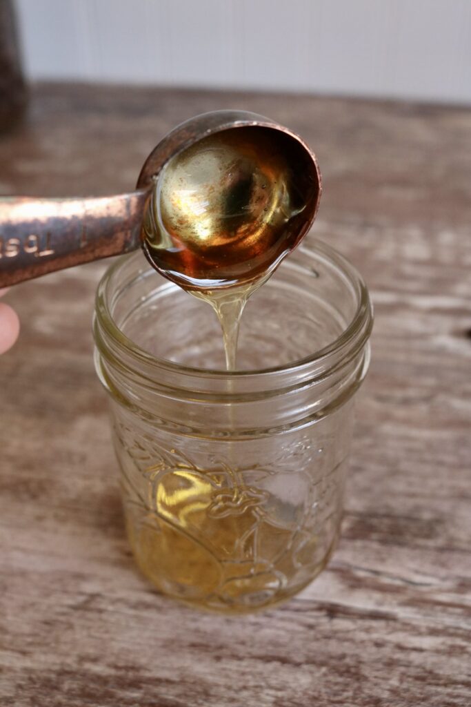 pouring a tablespoon of honey into a half pint jar