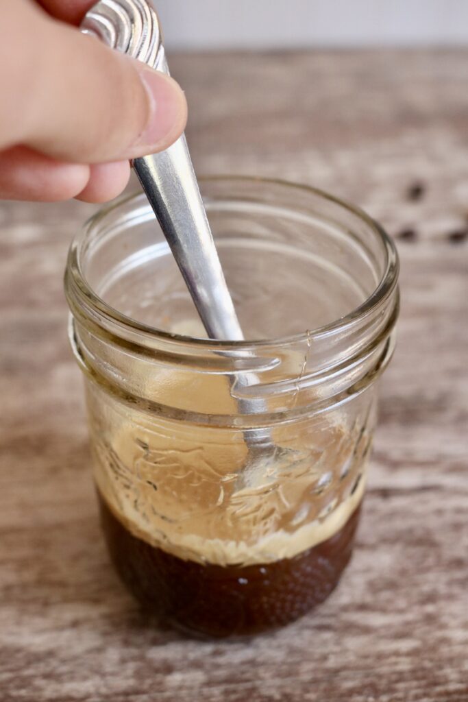stirring coffee mixture in a glass jar with a teaspoon