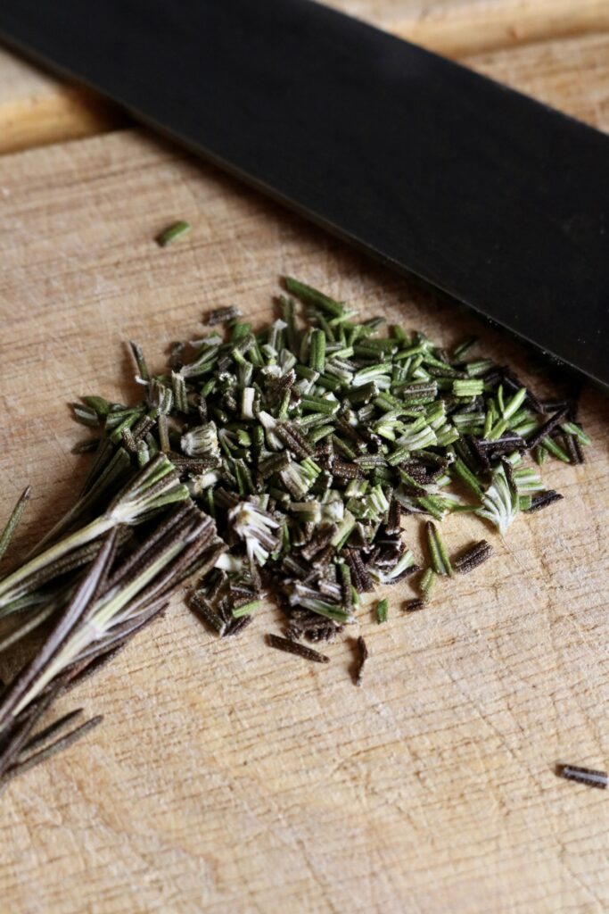 chopped rosemary on a wooden cutting board with a knife next to it