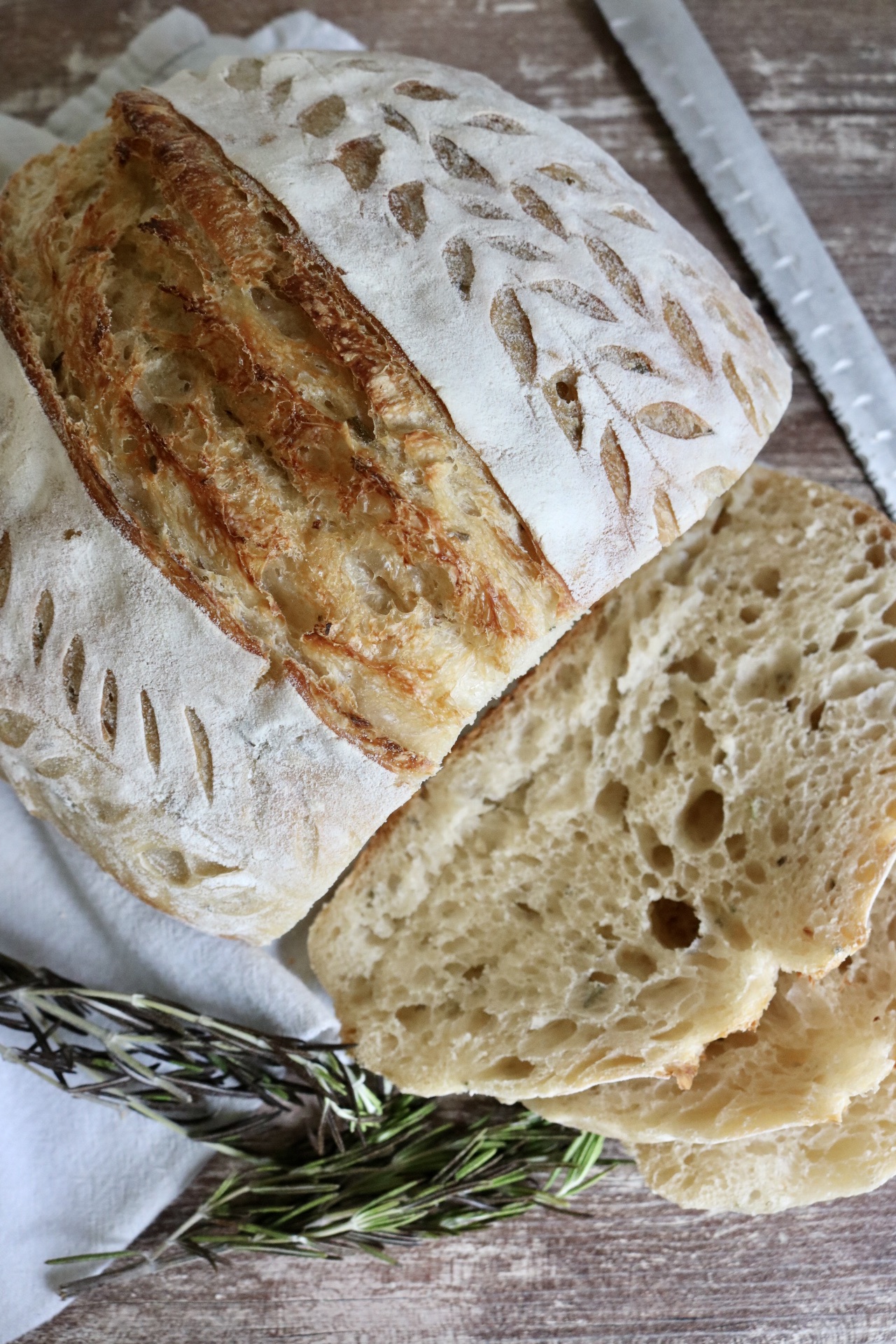 loaf of rosemary sourdough bread sliced with a bread knife