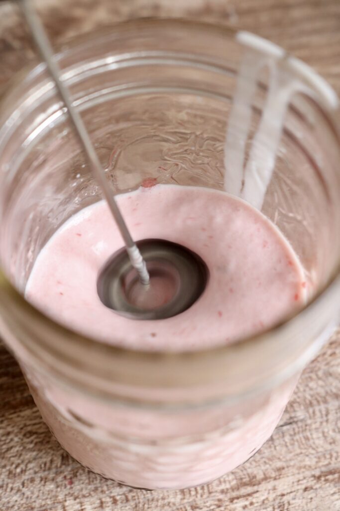 whipping strawberry cold foam in a jar with a handheld milk frother