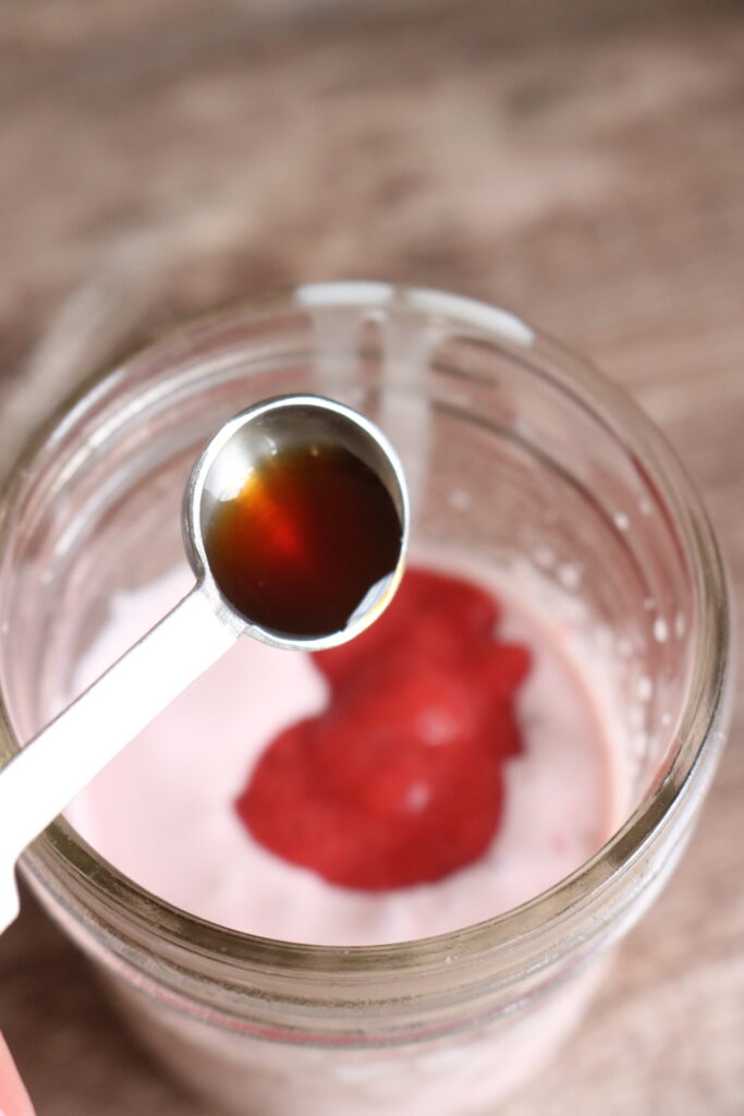 pouring vanilla extract into a jar with cream and strawberry puree in it