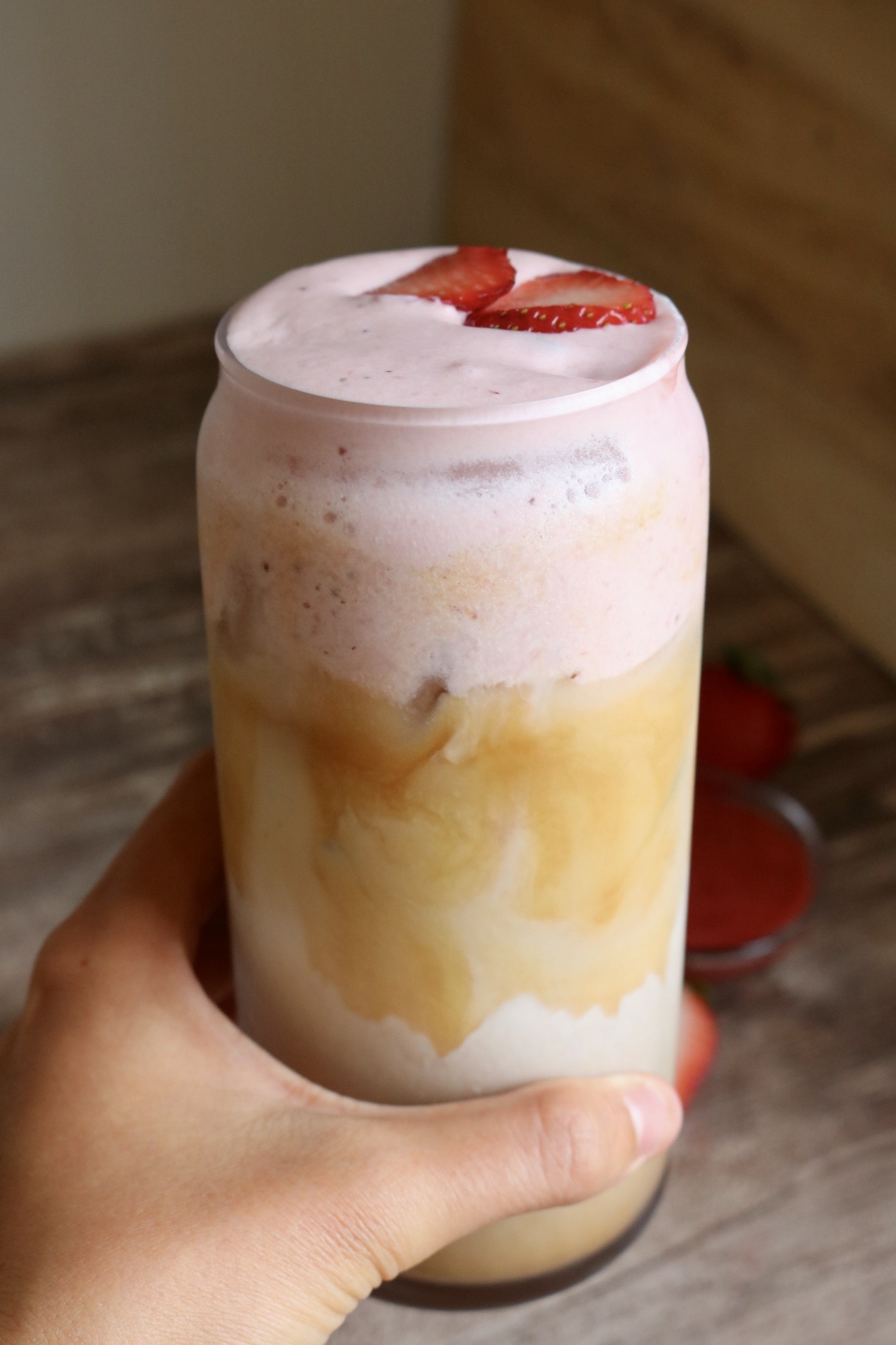 hand holding an iced latte with strawberry cold foam