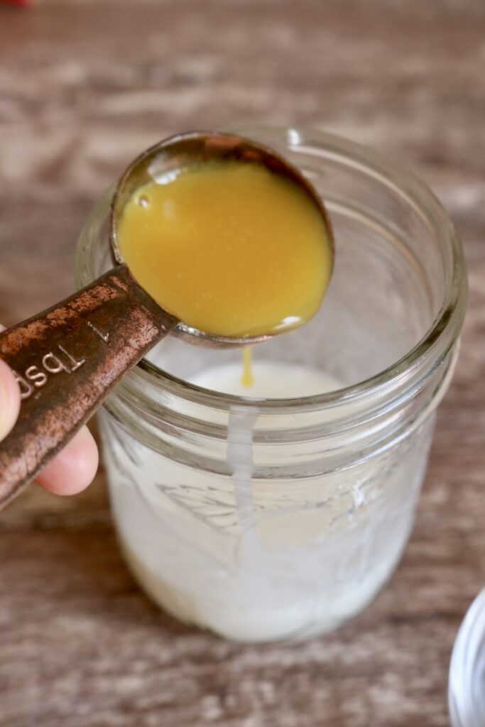 pouring a tablespoon of orange concentrate into a half pint jar with milk in it