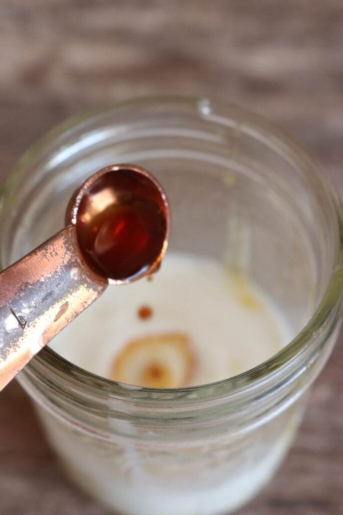 pouring vanilla extract into a small jar of milk
