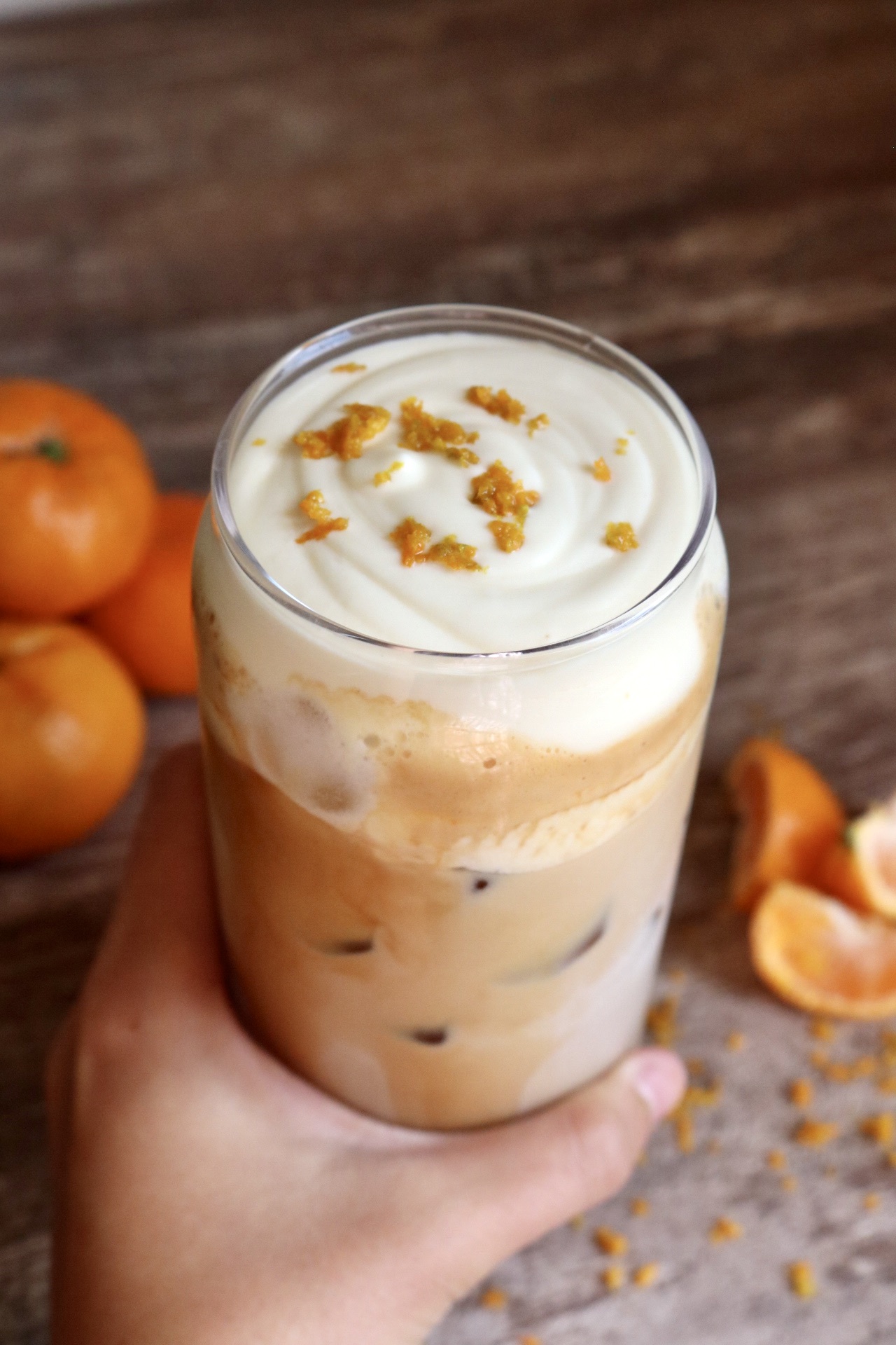 hand holding an iced latte with cold foam and orange zest on top