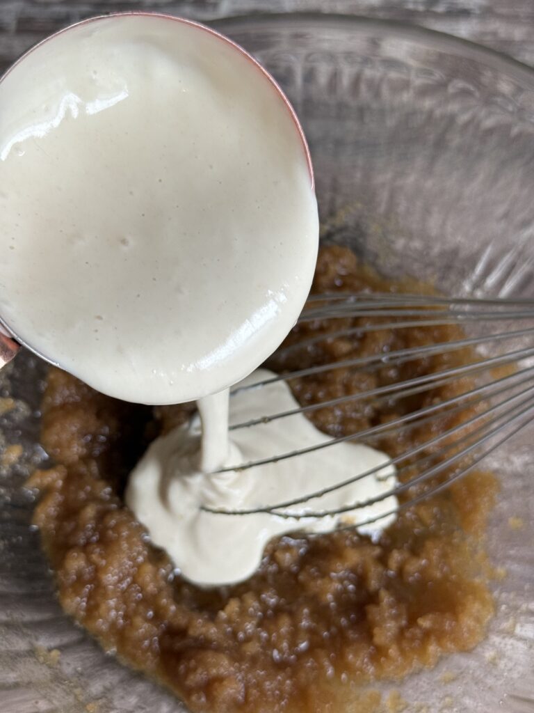 pouring sourdough starter into a bowl with melted butter and sugar mixture