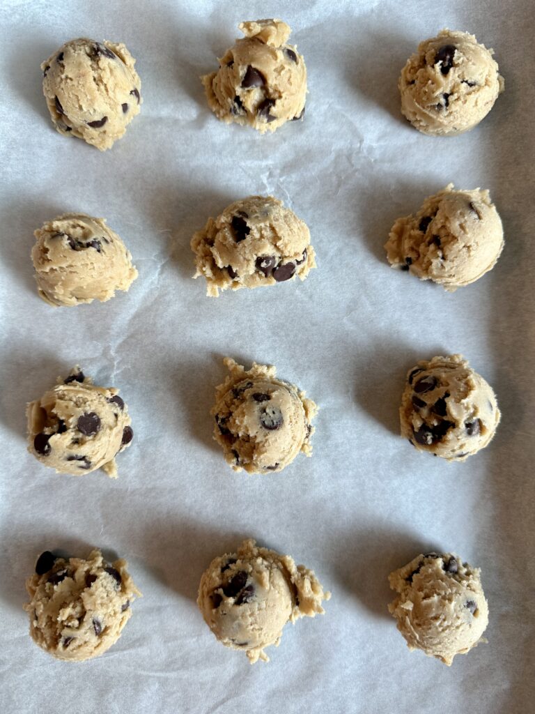 12 cookie dough balls on a parchment lined cookie sheet