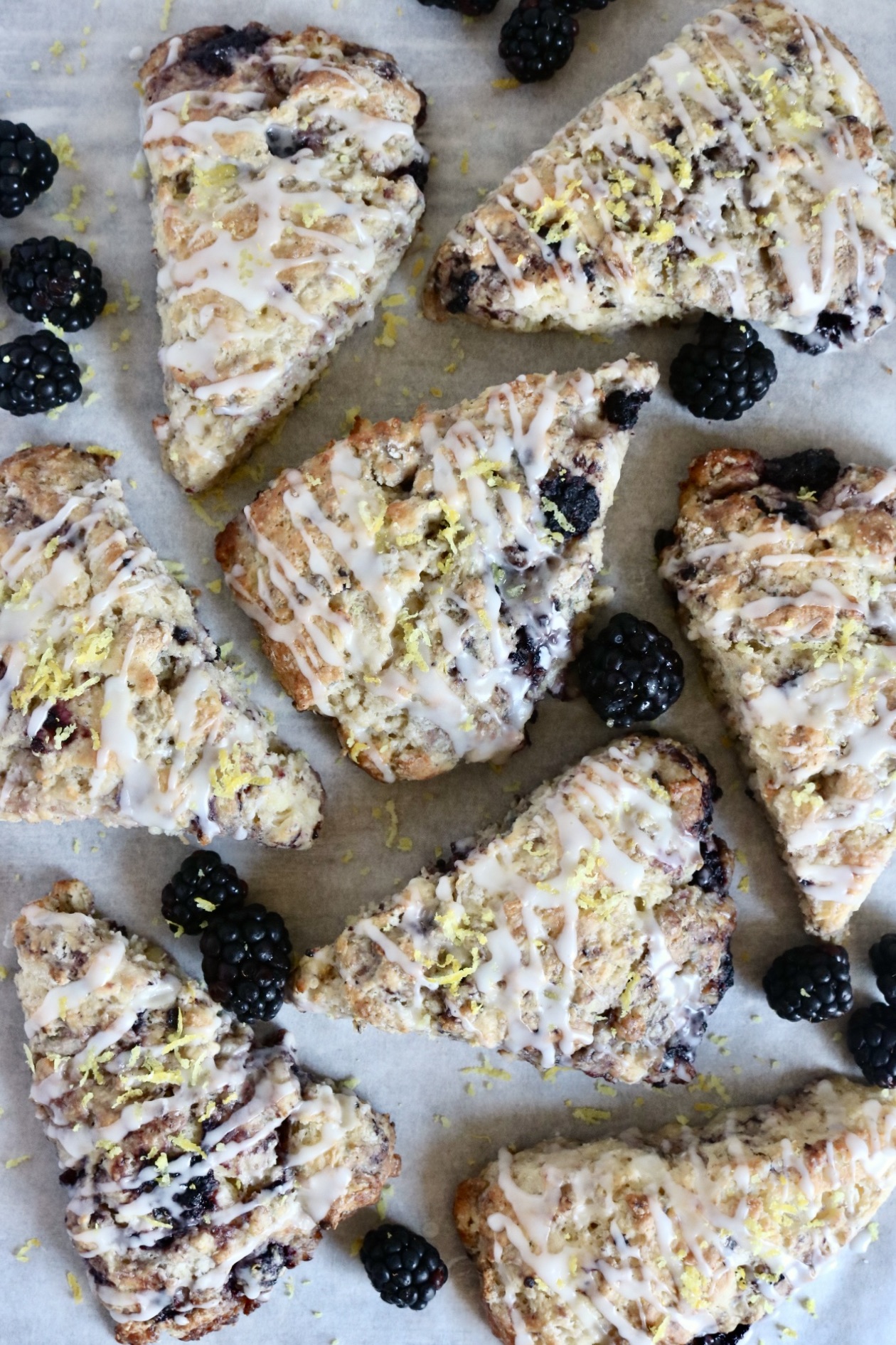 sourdough blackberry lemon sourdough scones randomly placed on a piece of parchment paper with blackberries scattered round