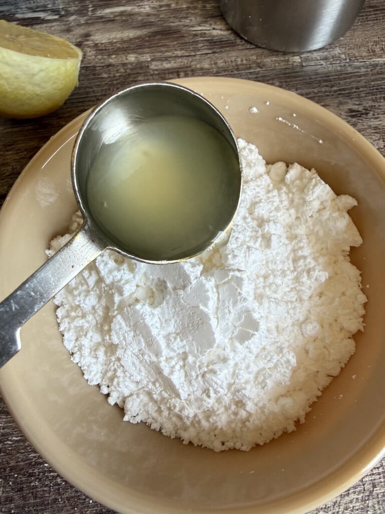 pouring 1 tablespoon of lemon juice into a small bowl of powdered sugar
