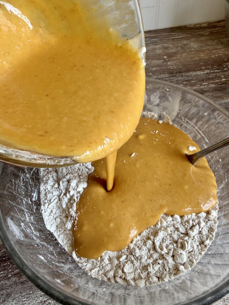 pouring pumpkin puree mixture into a bowl with flour
