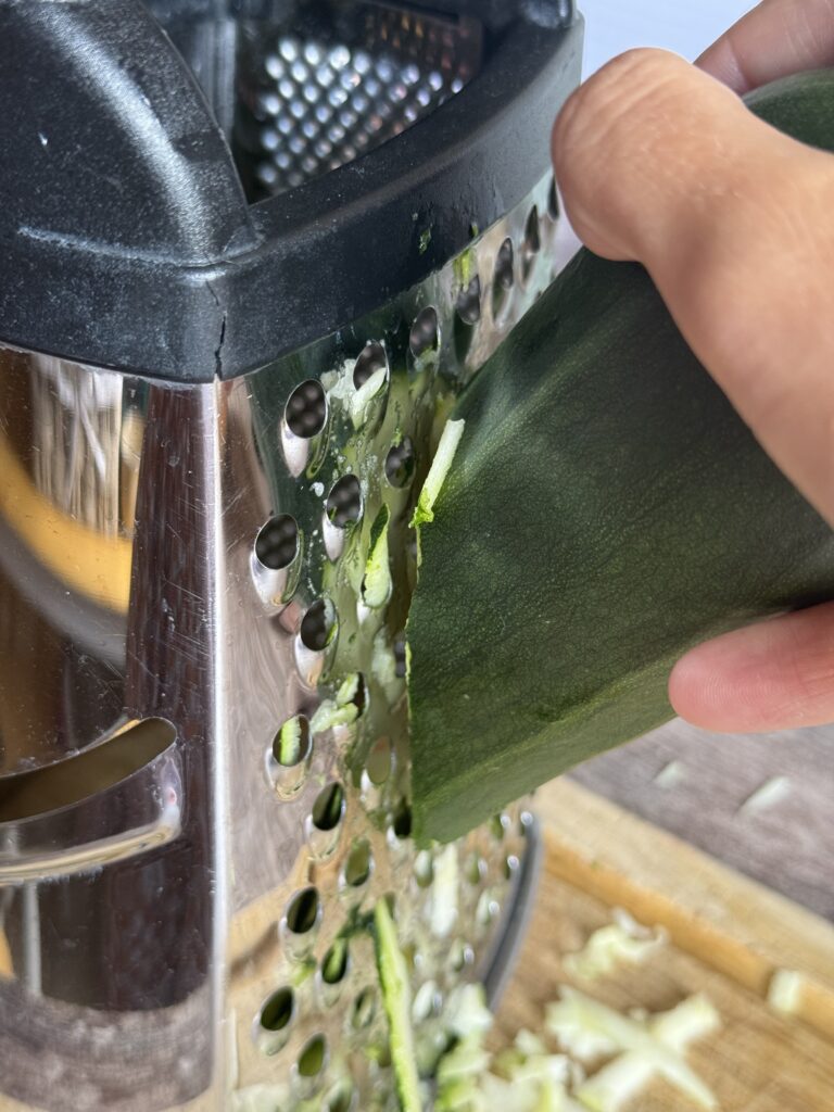 grating zucchini on a handheld cheese grater