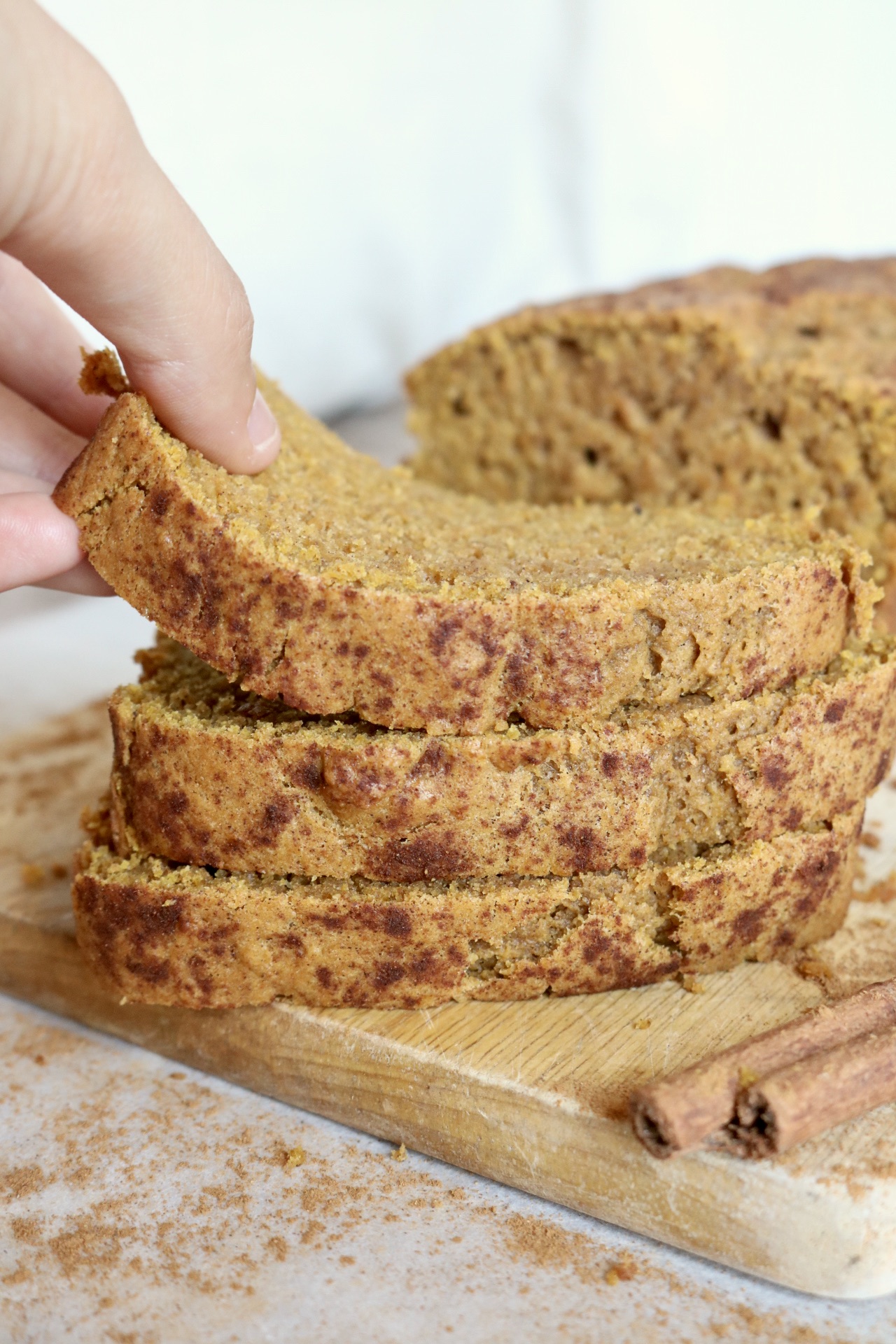 three slices of pumpkin bread on a wood board someone is picking up the top slice the remainder of the loaf is in the back round