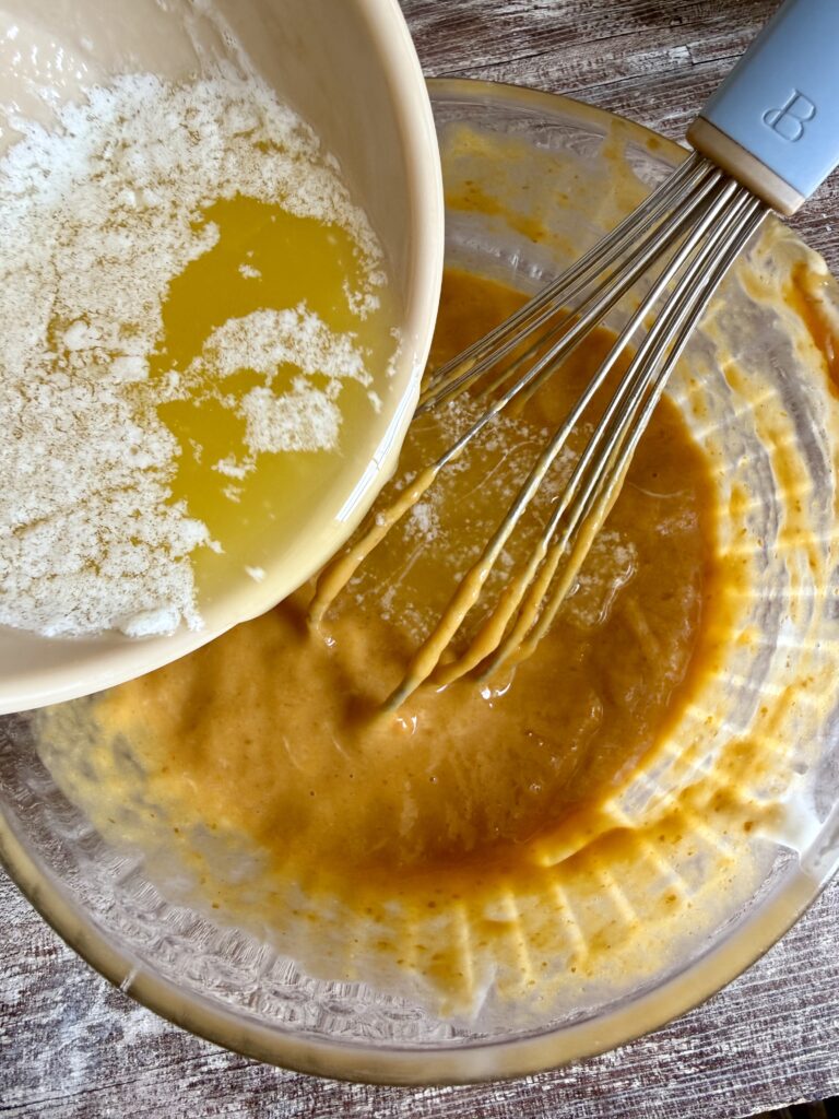 pouring melted butter into pumpkin puree ingredients a whisk is also in the bowl