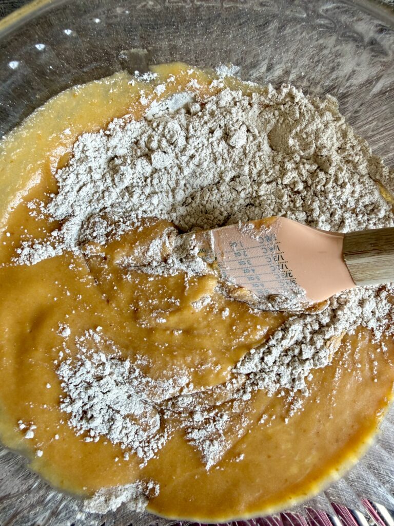stirring wet and dry ingredients for pumpkin bread together in a large bowl with a spatula