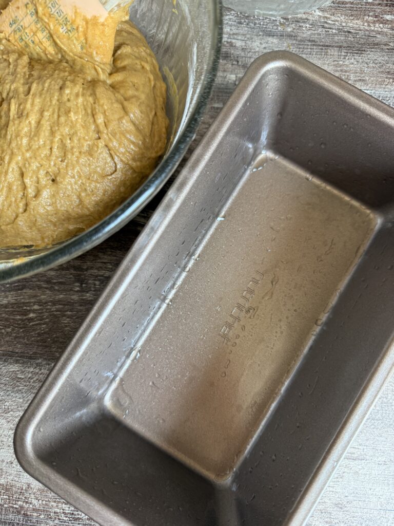 greased loaf pan with sourdough pumpkin bread batter in a bowl at the top left hand corner