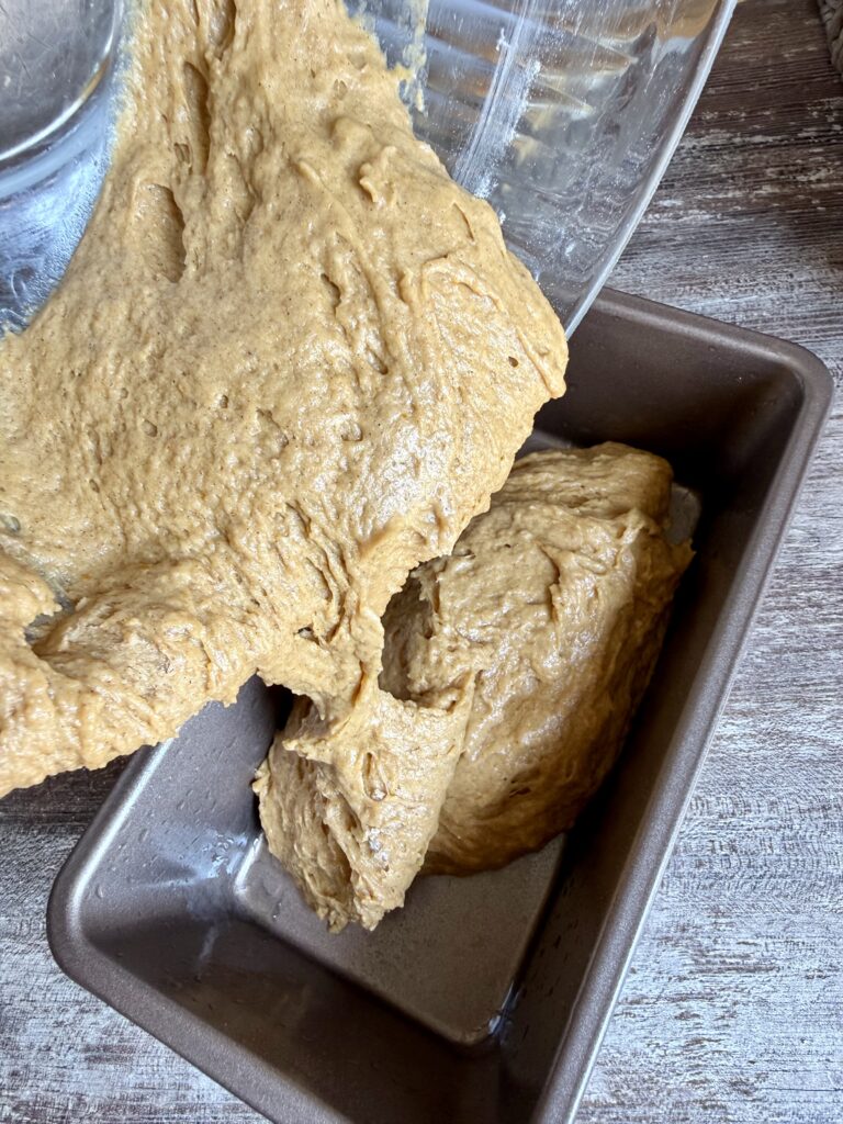 pouring sourdough pumpkin bread batter into a loaf pan