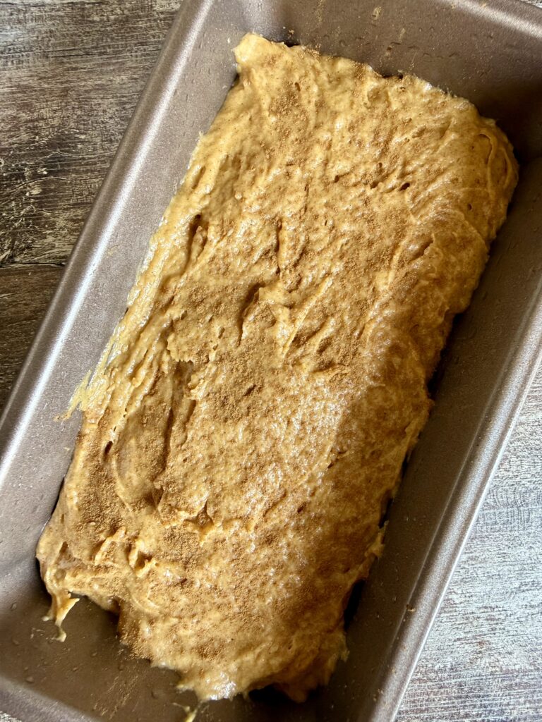 unbaked pumpkin bread in a loaf pan with cinnamon sprinkled on top